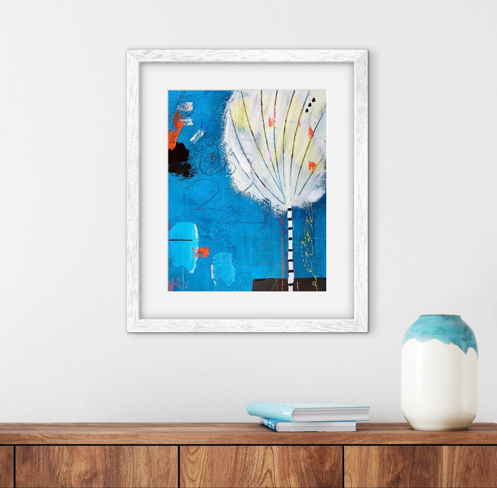 Framed abstract artwork on a wall above a wooden shelf with a vase and books.