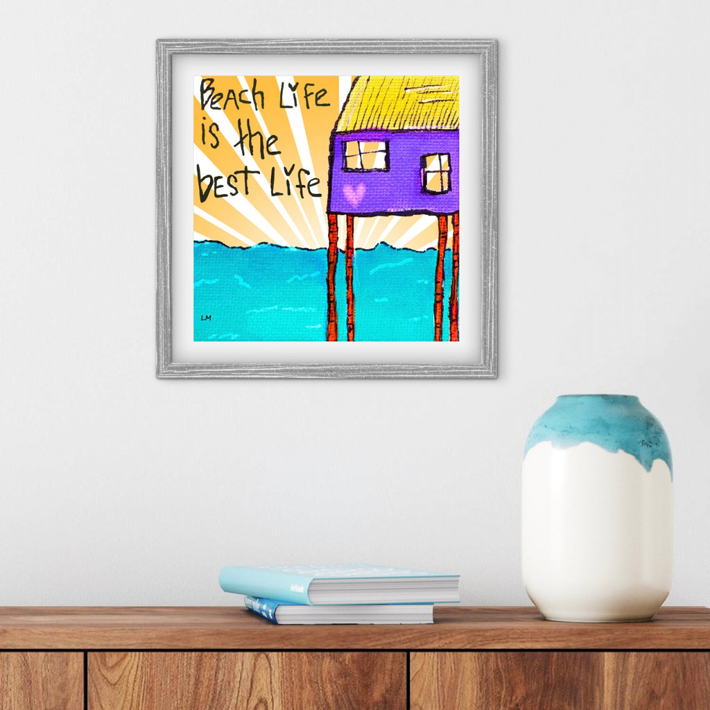 Framed artwork with a beach house design and 'Beach Life is the Best Life' text on a wall above a wooden shelf.