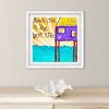 Framed artwork with a beach hut and 'Beach Life is the Best Lyfe' text on a white wall.