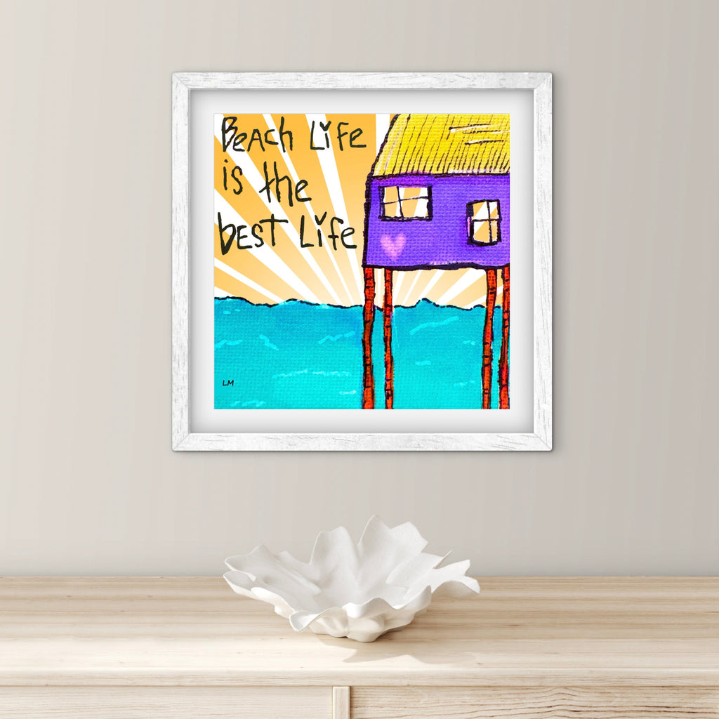 Framed artwork with a beach hut and 'Beach Life is the Best Lyfe' text on a white wall.