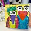 Colorful painting of two birds with a heart on a yellow background