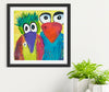 Framed colorful print of two whimsical birds on a white wall with plants below.