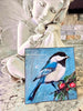 Bird and Berries acrylic painting, shown without a mat beside a white fairy figurine, featuring a blue, black and white bird with red berries