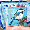 Bird and Berries 4x4 acrylic painting by Lori McKinnon, held in a paint-covered hand above a palette to show its size