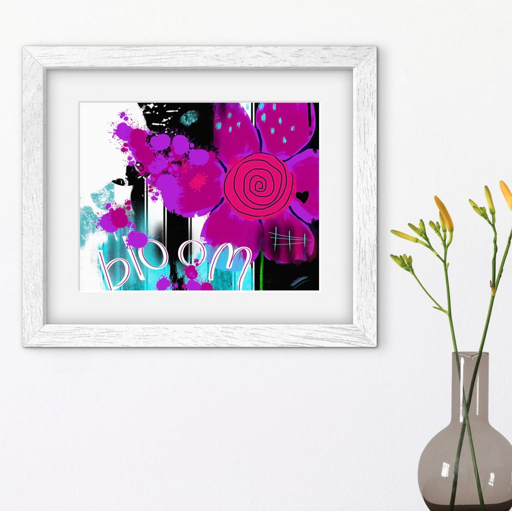 Framed abstract art with a pink flower and 'bloom' text on a white wall, next to a vase with greenery.