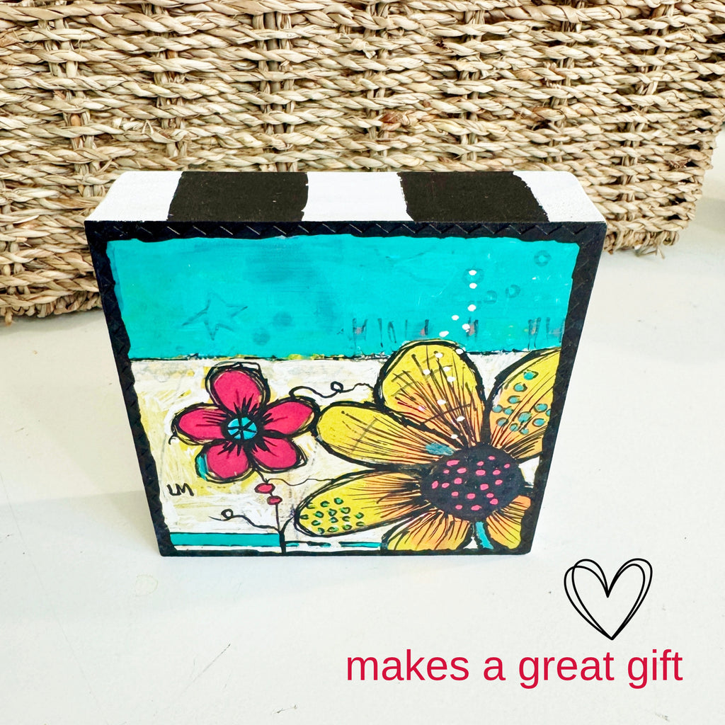 wood block painting on a white table with a basket behind it