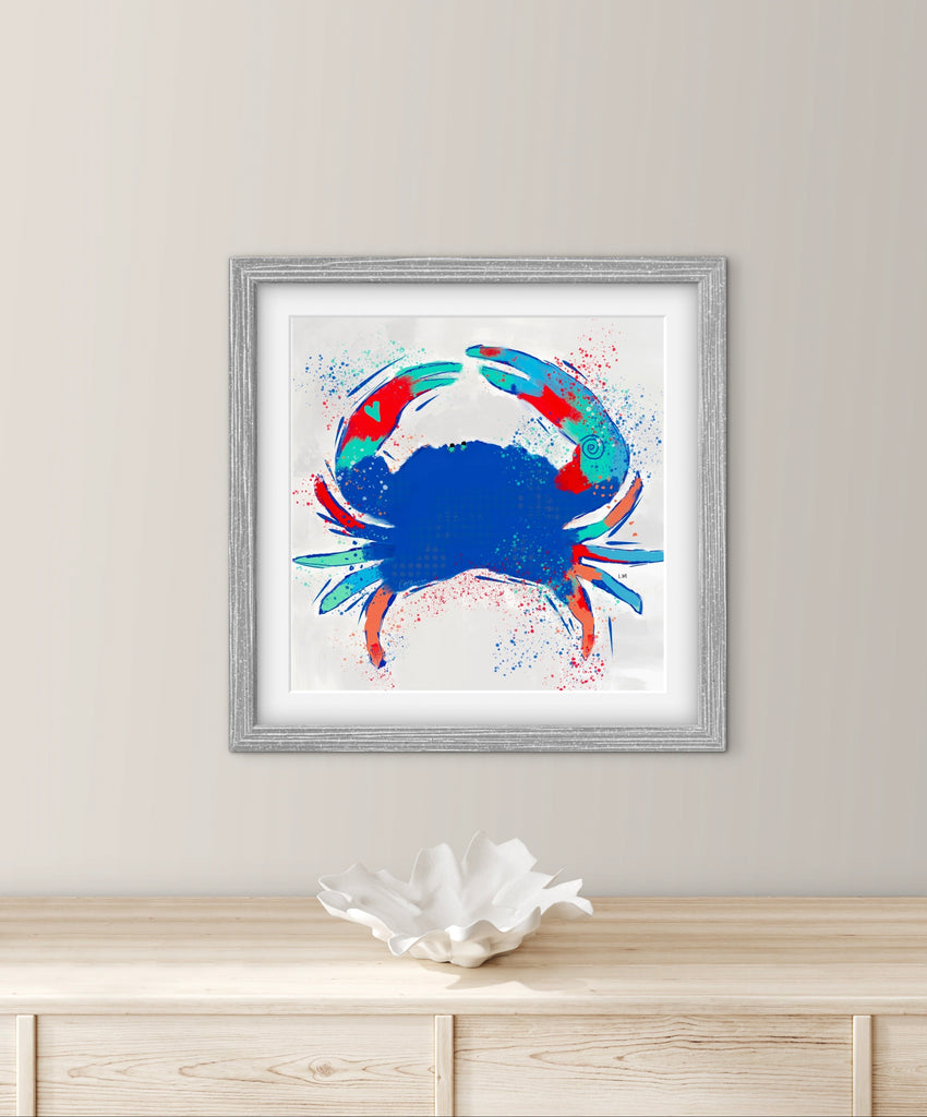 Framed artwork of a colorful crab on a white wall above a wooden surface.