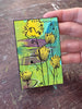 small floral painting held by a hand with a wooden surface in the background