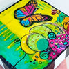 butterfly painting on a wood block with vivid colors of yellow, green, pink and blue