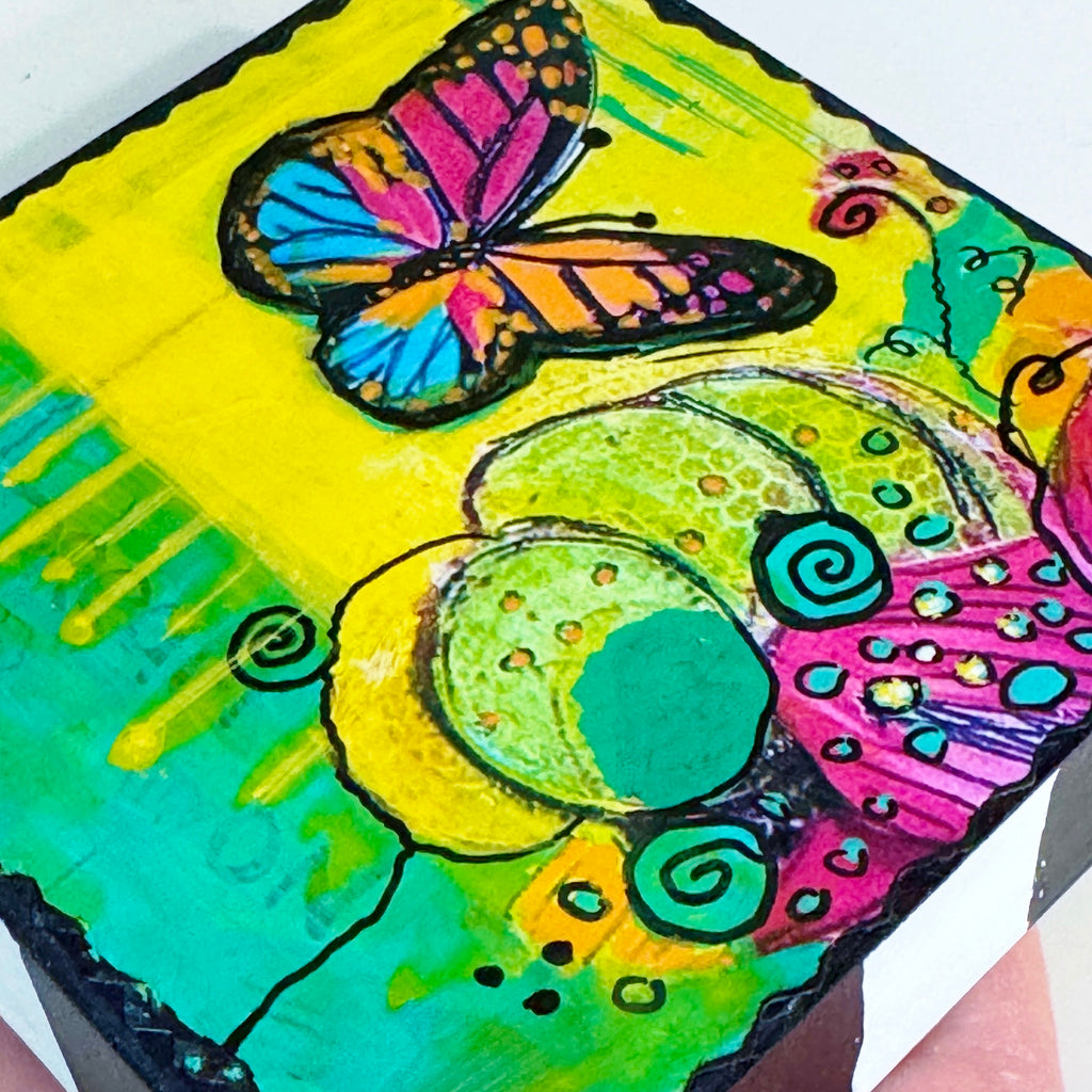 butterfly painting on a wood block with vivid colors of yellow, green, pink and blue