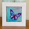 A butterfly painting in a white mat standing on a table with vases behind it