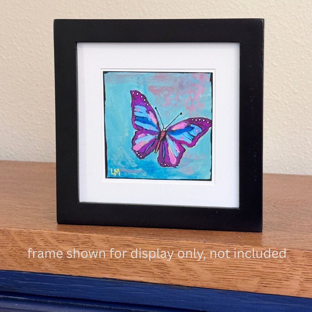 A butterfly painting in a black frame with a white mat standing on a table with text below it 'frame shown for display only, not included'