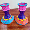 A pair of hand-painted  candle holders on a wooden table against a plain wall.