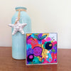 Cheer Up floral art block displayed on a wooden surface beside a pale turquoise vase decorated with a white starfish