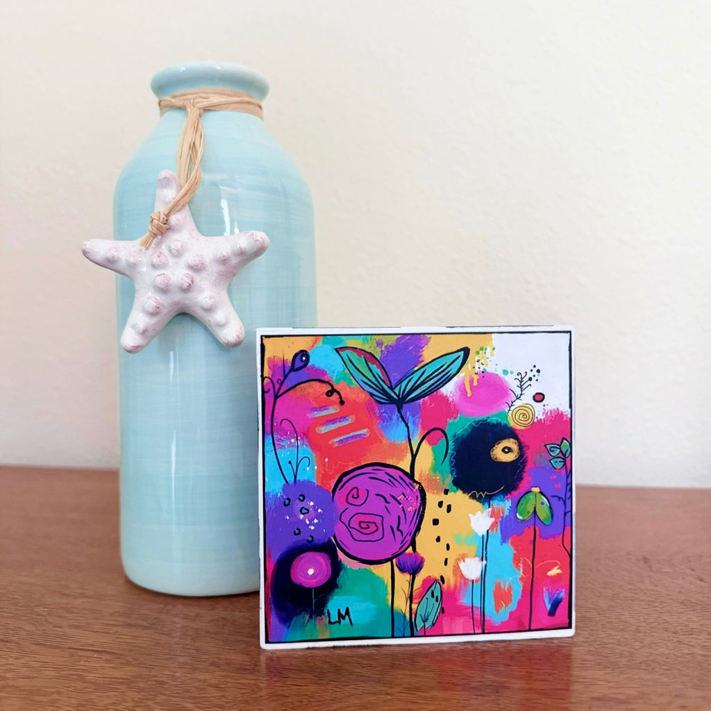 Cheer Up floral art block displayed on a wooden surface beside a pale turquoise vase decorated with a white starfish