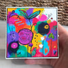Cheer Up art block held in a hand, featuring colorful abstract flowers and leaves in pink, purple, turquoise, yellow, and orange.