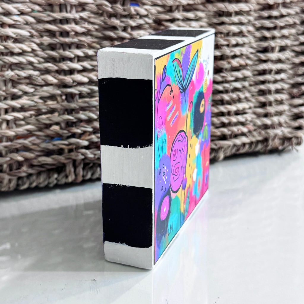 Side view of Cheer Up art block showing its black-and-white striped painted edge and a partial view of the colorful floral artwork