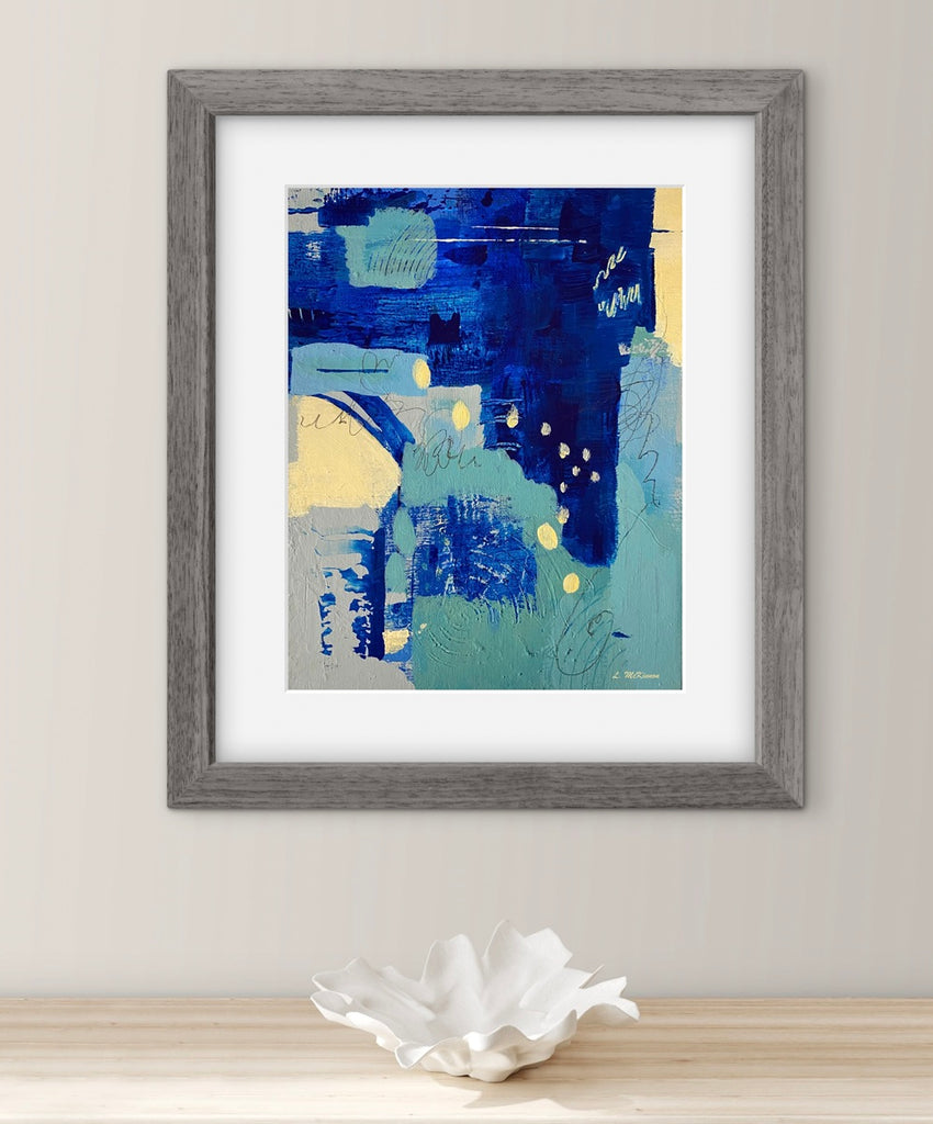 Framed abstract art print with blue and yellow colors on a white wall.