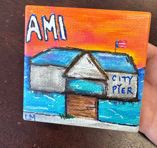 coaster with a pier and text saying "AMI City Pier" held by a hand on a table