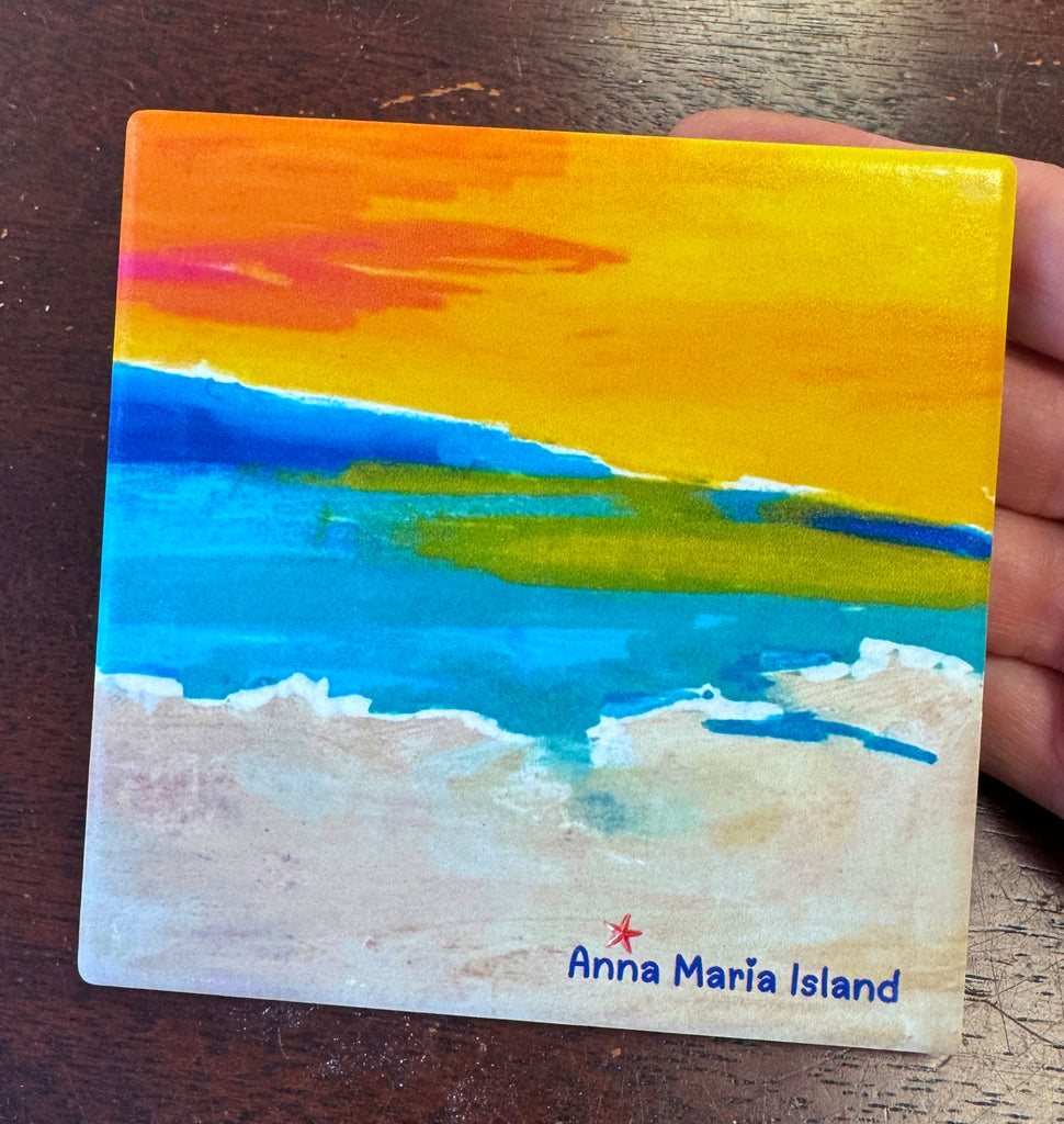 A square coaster featuring a beach scene with a yellow-orange sky, blue water and pale sand. The text 'Anna Maria Island' with a small starfish appears at the bottom.