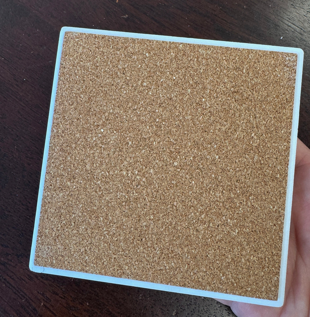 back of a coaster with cork backing held by a hand over a dark tabletop