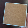 a hand holding a coaster to show the backside with a cork bottom. Pictured over a dark table top