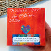 Orange-painted back of A Colorful Day art block, titled and signed by Lori McKinnon, dated 2026, with a colorful heart and artist label.