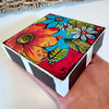 A Colorful Day floral art block resting flat in a hand, showing its vibrant flower design and black-and-white striped edges