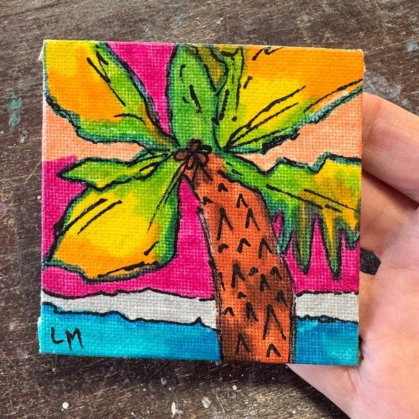 A small square canvas painting of a palm tree with bright yellow, green, orange, pink, blue, and brown colors, held by a hand over a dark wooden surface.