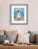 Framed artwork of a bird on a beach. Framed and hung on a wall above a sofa with cushions.