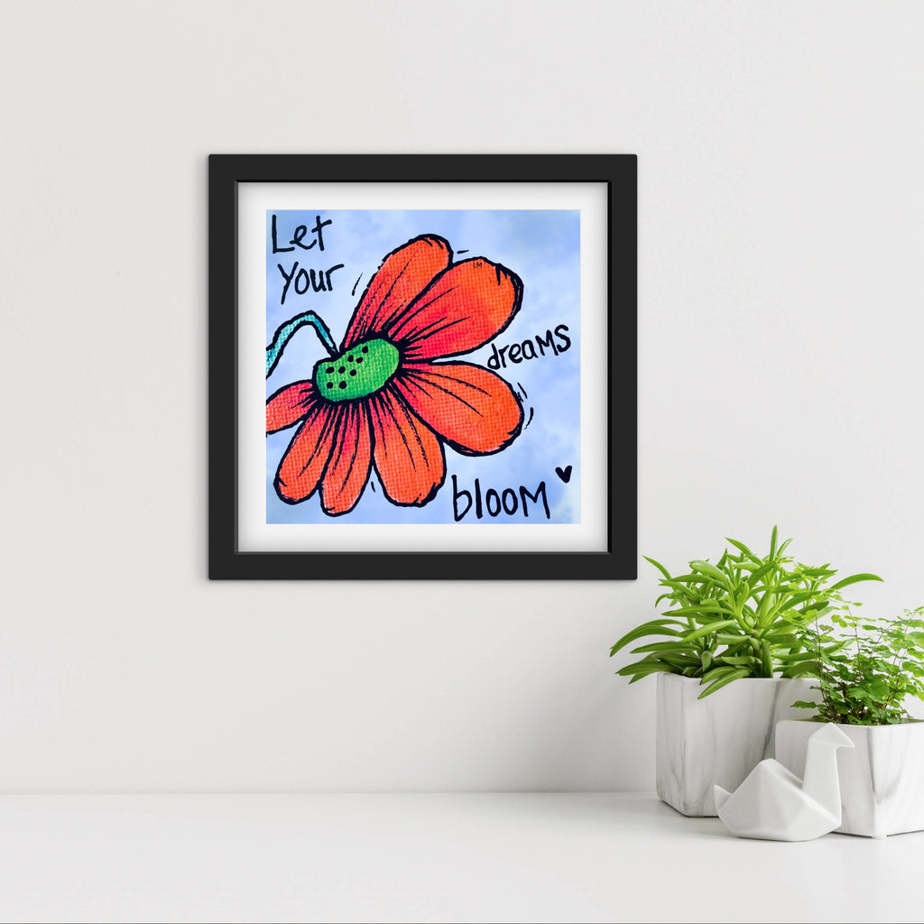 Framed artwork with a red flower and motivational quote on a white wall with plants below.