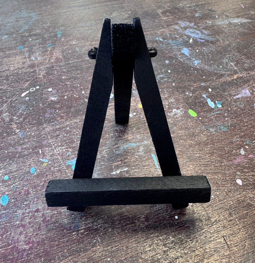 small black easel made of wood photographed on wooden table with paint splatter