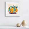 Framed abstract pumpkin art print on a wall with decorative vases below.