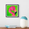 Framed artwork of a pink flamingo on a green background, placed on a wooden surface with books and a vase.
