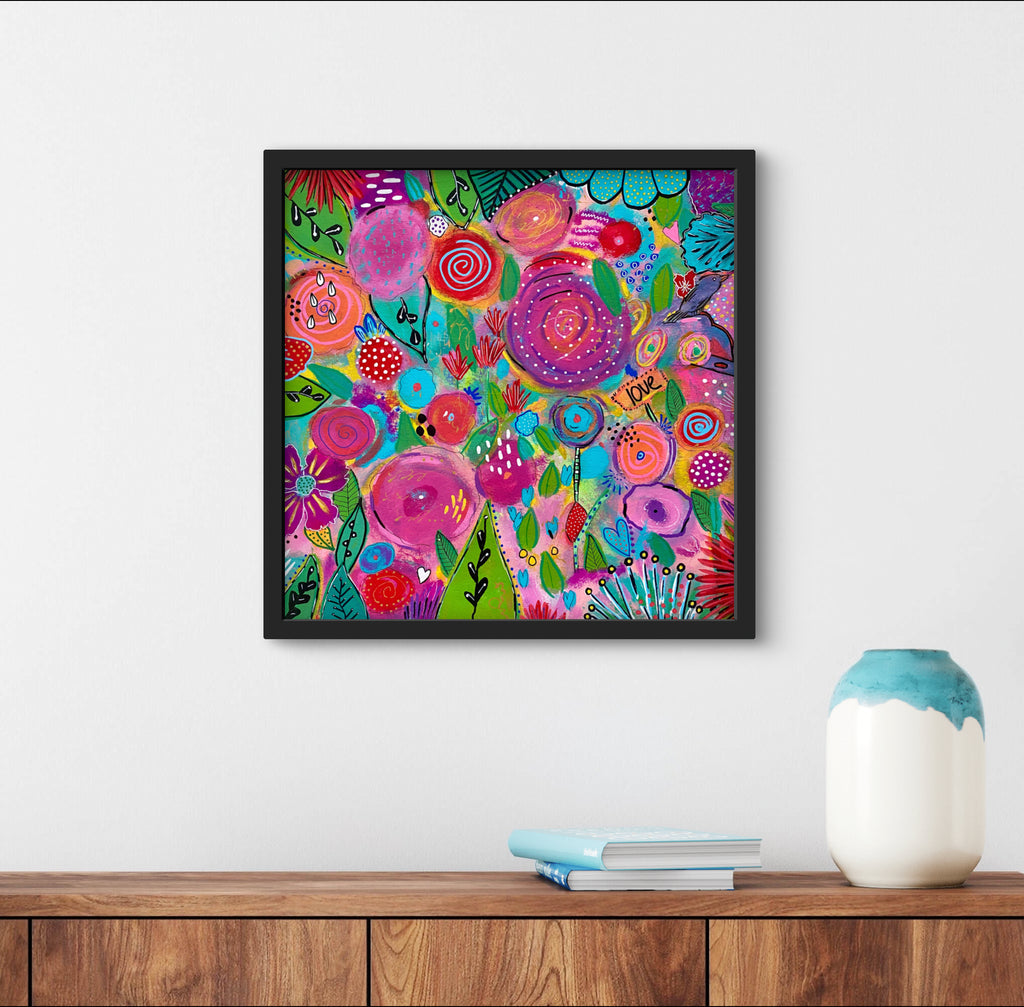floral painting in black frame n a white wall above desk with books and vase