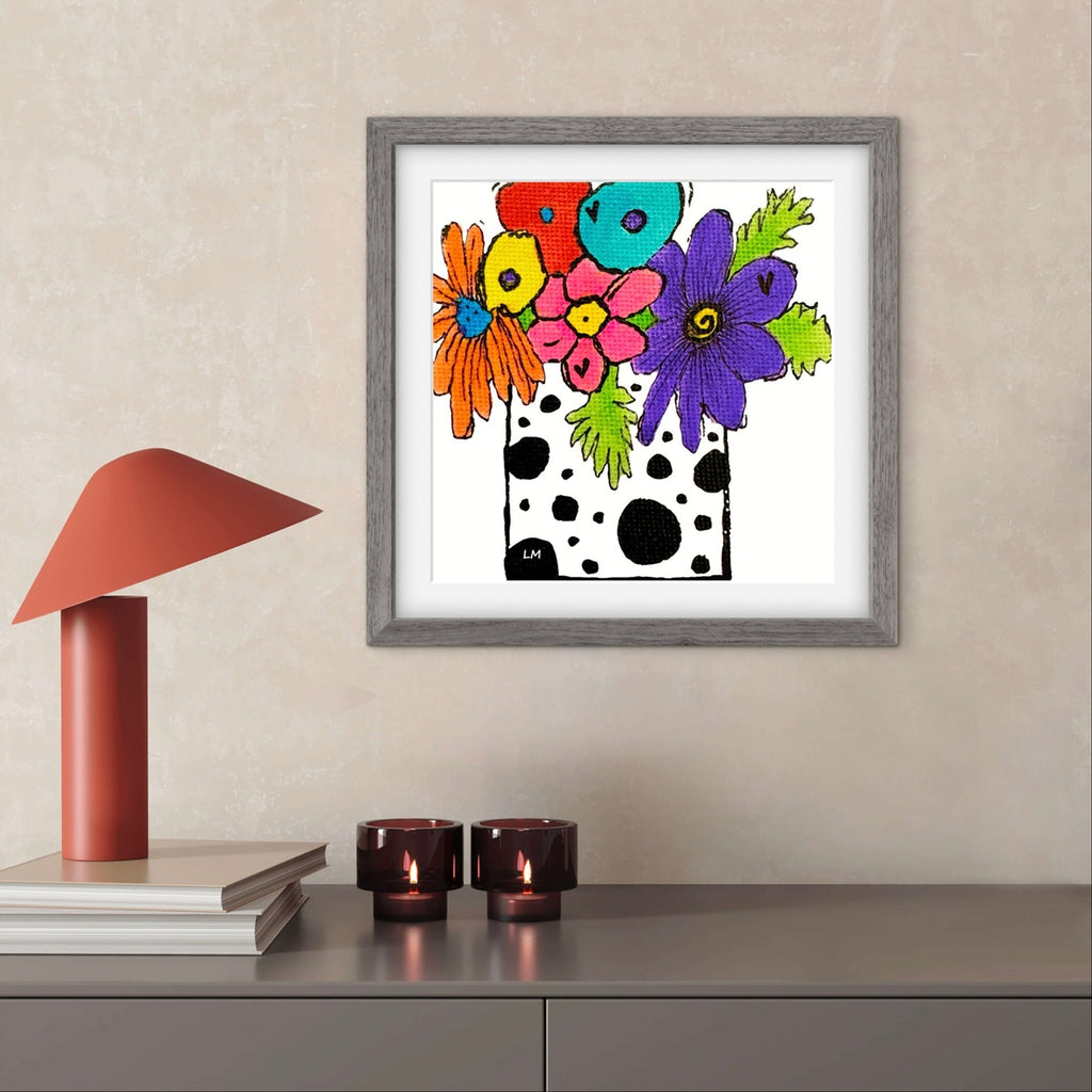 Framed colorful floral artwork on a wall above a shelf with decorative items.