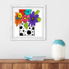 Framed colorful floral artwork on a wall above a wooden shelf with a vase and books.