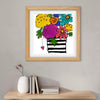 Framed artwork of colorful flowers and a striped vase on a gray wall with a shelf below.