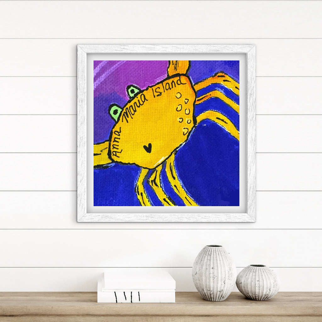 Framed artwork of a yellow creature with a purple and blue background on a white wall.