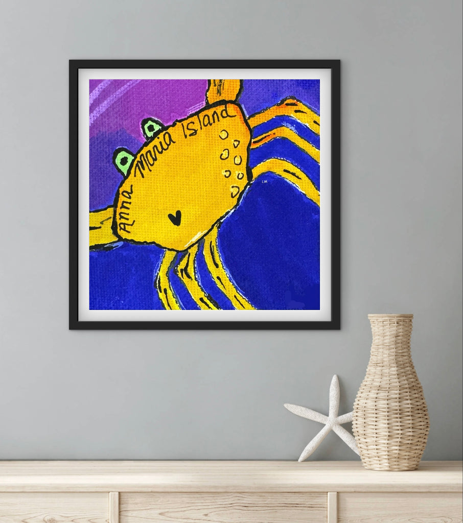 Framed artwork of a yellow crab on a blue background, displayed on a wall with a vase and starfish below.