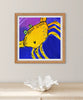 Framed artwork of a yellow crab with 'Alma Maria Island' text on a purple background, displayed on a shelf.