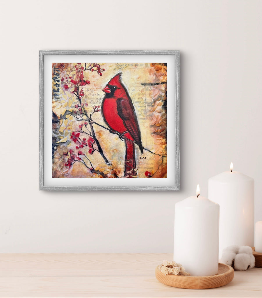 Framed artwork of a red cardinal bird on a branch with berries, displayed on a wall above a wooden surface with candles.