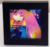 A framed abstract art print featuring a large pink shape, a white flower, and some shades of blue presented in a black square frame against a light background