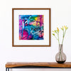 an abstract piece hanging on a white wall over a wooden  table. Art is shown with a white mat and a brown frame