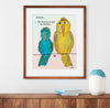 Framed artwork of two whimsical birds on a wire with a quote, displayed on a wall above a wooden shelf.