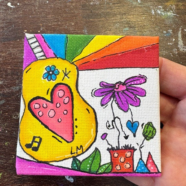 A small square canvas painting held by a hand, featuring a colorful doodle-style design with a yellow guitar, pink heart, purple flower, rainbow stripes, and green leaves on a rustic wooden background.