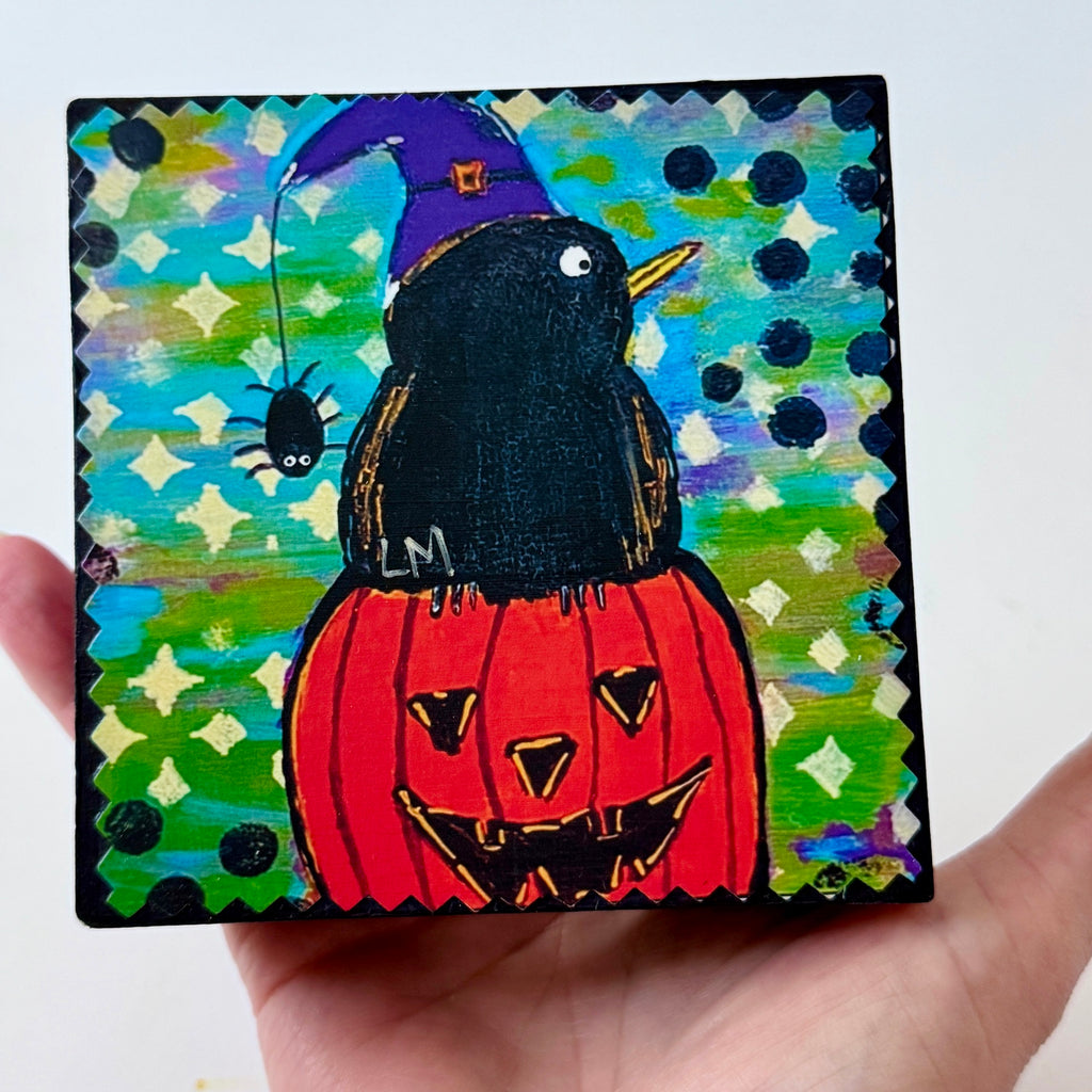 a small painting being held by a hand. the artwork has an abstract background and features a fun Halloween pumpkin, crow and small spider