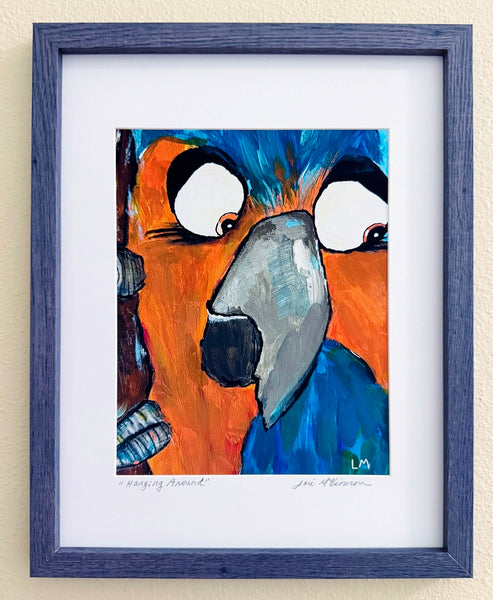 orange and blue parrot in a blue-gray frame with a white mat against a beige background