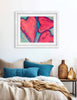 Framed abstract art above a bed with pillows and a vase.