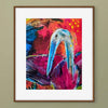 A framed abstract artwork of a blue heron with a long beak, set against a vibrant background of red, pink, and blue brushstrokes. The artwork is presented in a white mat and a brown wooden frame, mounted on a solid sage green wall.
